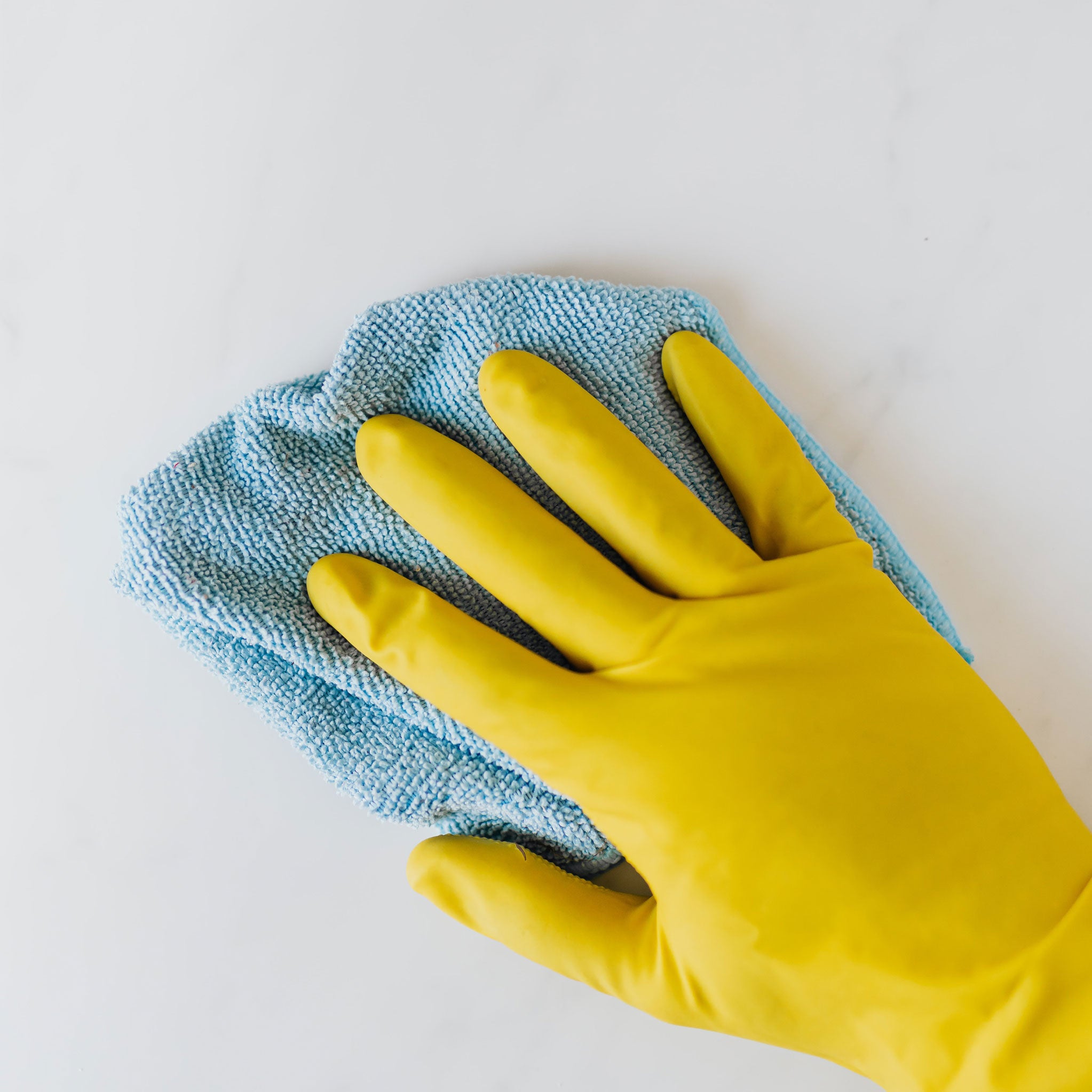 Hand med gul diskhandske som rengör en yta