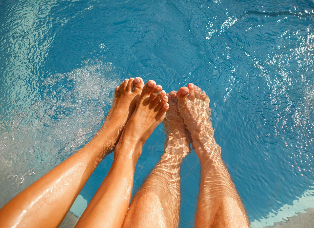 Ett par som badar fötterna vid poolkanten